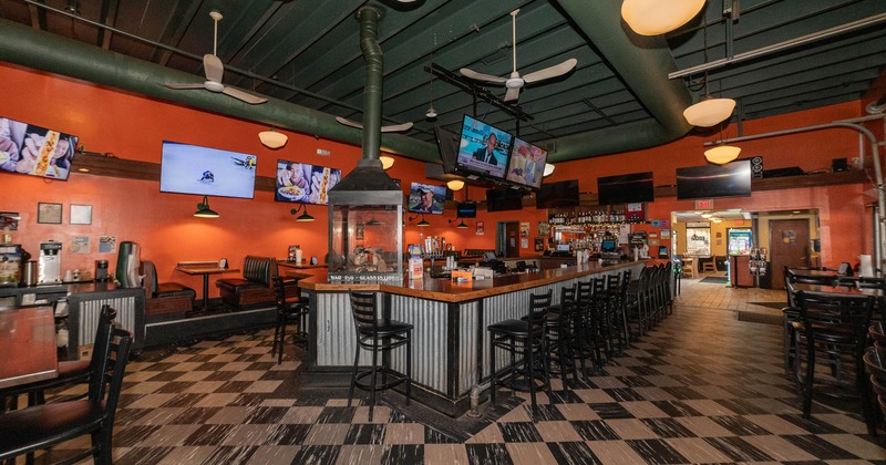 Interior with a long bar, wooden chairs and black and white tiles floor.