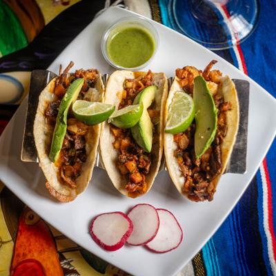 Surf and turf tacos with avocado, radish slices, dipping sauce and lime wedges.