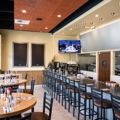 Interior view of a restaurant with a bar, tables, and a television displaying a sports game.
