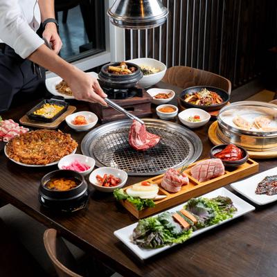 A full table and a hand grilling meat on the grill in the middle.