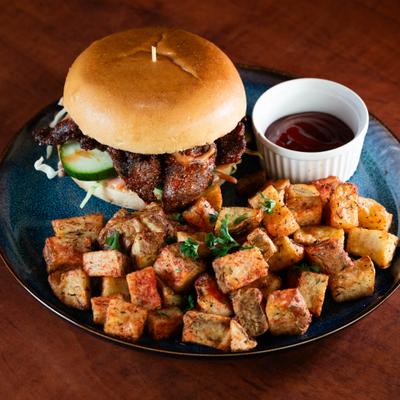 A burger served on a plate with a side of roasted potatoes and a small dish of sauce.