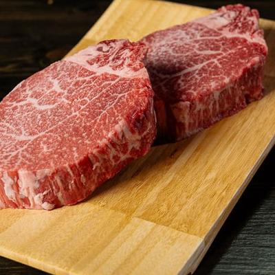 Two marbled steaks rest on a wooden board.