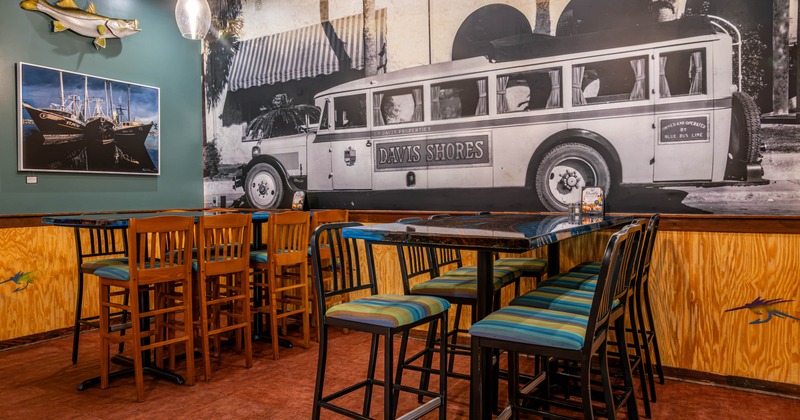 Interior of a dining area featuring tall barstools, a black table, mural, and fishing themed decor