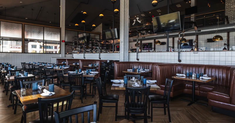 Interior of a modern restaurant with a bar, leather booths, pendant lights, and wall-mounted TVs
