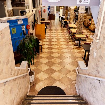 Staircase leading to a dining area with checkered tile flooring, tables, chairs, and booths.