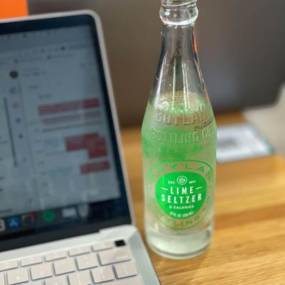 A laptop and a bottle of Lime seltzer on a table, close up.