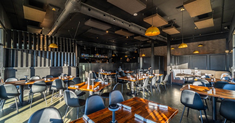 Modern restaurant interior with wooden tables, black chairs, and yellow pendant lights