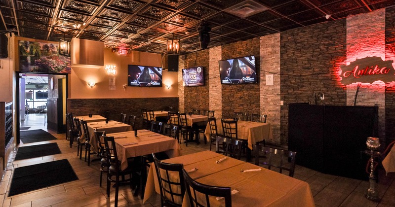 Interior, dining area, tables for four ready for guests, TVs on the wall, ''Antika'' neon sign