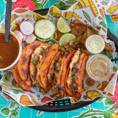 Quesabirrias served with a side of consome, fresh garnishes and dipping sauces.