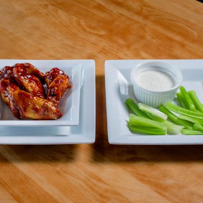 Plate of wings served alongside plate with celery sticks and a dip.