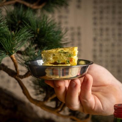 Hand holding a small bowl with egg omelette.