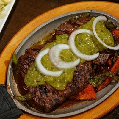 Skirt steak with peppers and tomato, topped with green sauce and raw onions.