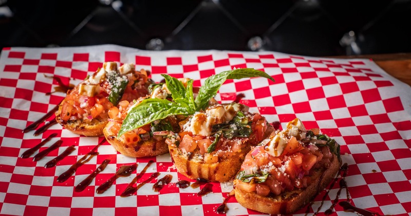 Four crispy bruschetta slices with tomatoes, cheese, basil, and balsamic glaze