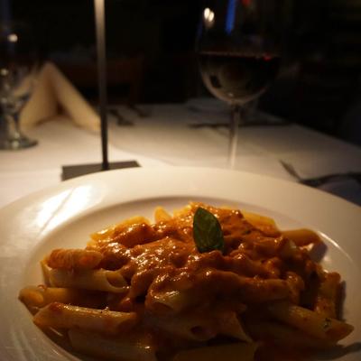 Penne pasta in tomato cream sauce and a glass of red wine under warm lighting.