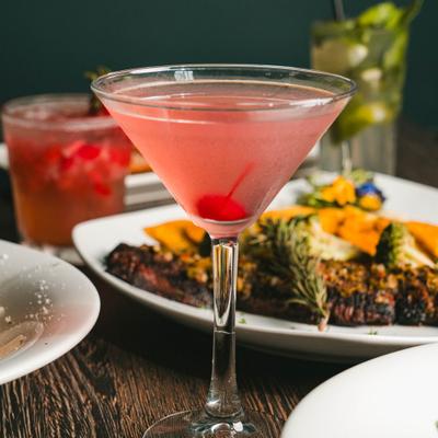 Cosmopolitan cocktail garnished with a cherry and served alongside various dishes.