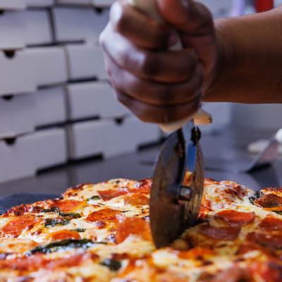 An employee cutting a pizza, hands close up.