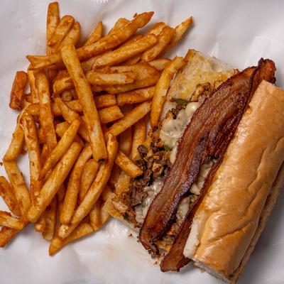 Philly cheesesteak sandwich with bacon, served with fries.