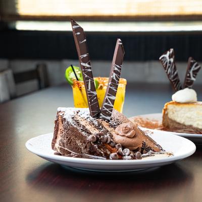 Slice of chocolate espresso cake served on  a table with cheesecake and a cocktail.