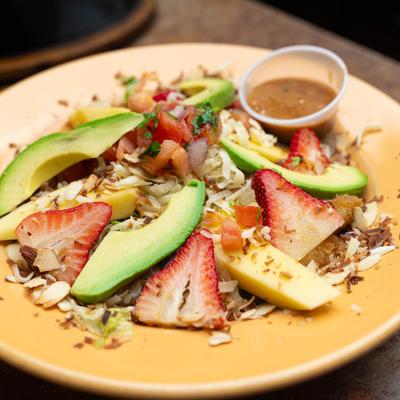A salad with strawberries, avocado, mango, coconut, and nuts.