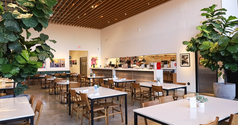 Interior, dining area, tables for four, kitchen in the back, large plants with pots as decoration