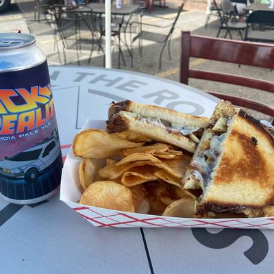 A grilled cheese sandwich served with potato chips, alongside a can of beer.
