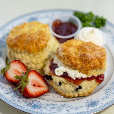 Two scones filled with jam and cream served with strawberries and extra jam and whipped cream.