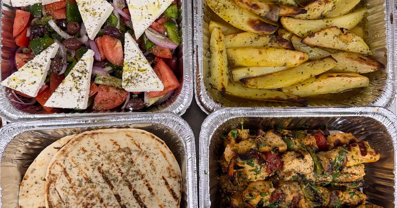 Catering trays with chicken skewers, popatoes, pita bread and Greek salad