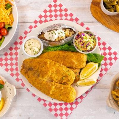Fried fish fillet, with coleslaw, baked potato, and tartar sauce, top view.