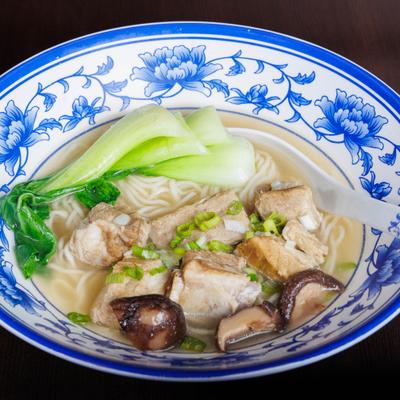 Noodle soup with ribs, bok choy, mushrooms, and scallions in a blue floral bowl.