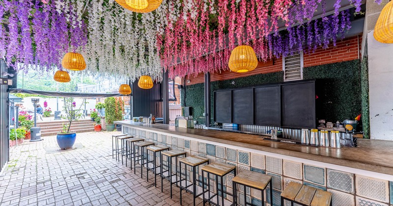 Vibrant outdoor bar with a tiled counter, stools, potted plants, and a floral ceiling