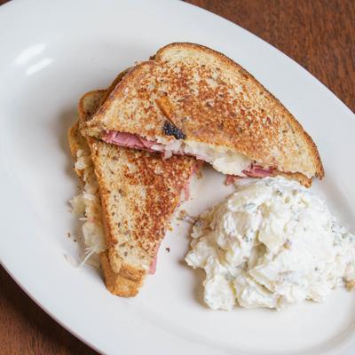 Rueben Sandwich served with a side of potato salad on a white oval platter.