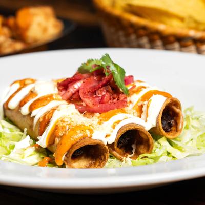 Smoked Mahi Mahi taquitos, with pickled onions, cheese, sour cream, and lettuce.