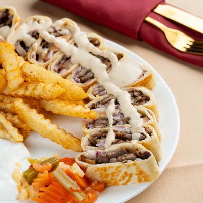 Sliced beef shawarma wrap with creamy sauce drizzle served with seasoned fries and pickled veggies.