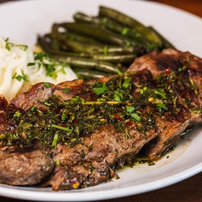 Steak topped with scallion chimichurri, served with mashed potatoes and green beans.