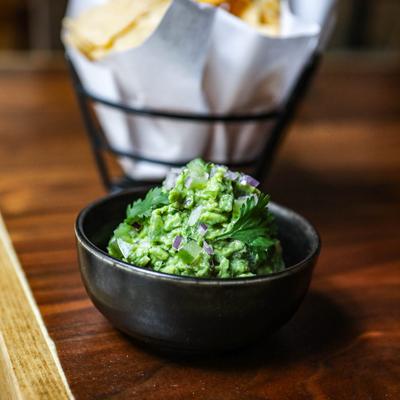 Fresh guacamole in a black bowl with chips in the background.