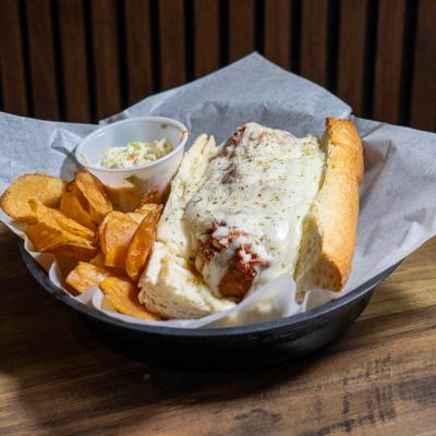 Meatball grinder topped with melted mozzarella cheese, served alongside chips and coleslaw.