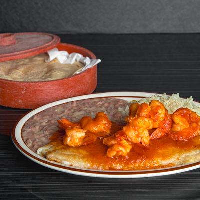 Fish and shrimp in a spicy sauce, served with rice and refried beans on a plate.
