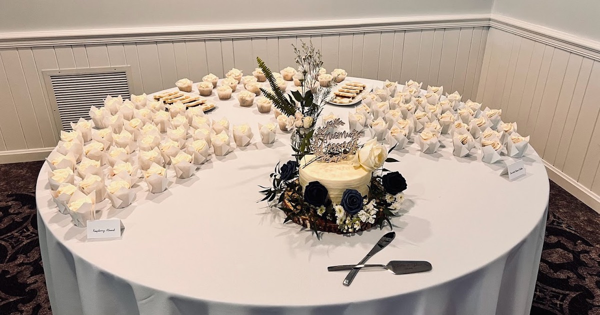 A round table with cupcakes and a small wedding cake.