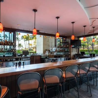 Stylish bar with wooden counter, black mesh chairs, and hanging orange lights.