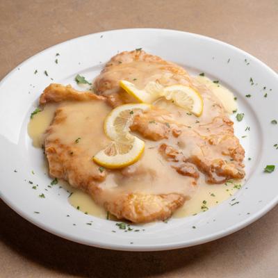 Chicken Francese garnished with lemon slices and herbs.