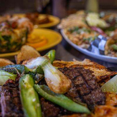 Steak fajitas, blurred dishes in the background.