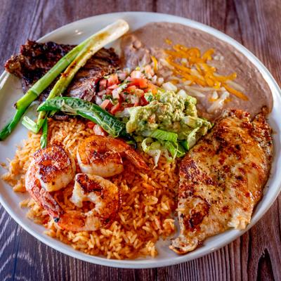 Grilled chicken, shrimp, steak, rice, beans and guacamole on round plate.