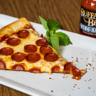 Slice of pepperoni pizza with a bottle of wing sauce