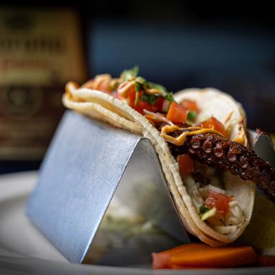 Octopus taco topped with diced tomatoes and spicy mayo, served on a metal holder.