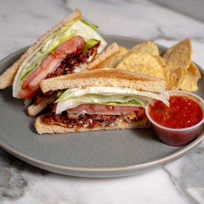 BLT sandwich with sides of chips and dipping sauce, served on the table.