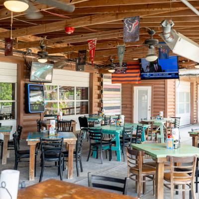 Covered patio with table seating, exposed wood beams with fans and TV sceers.