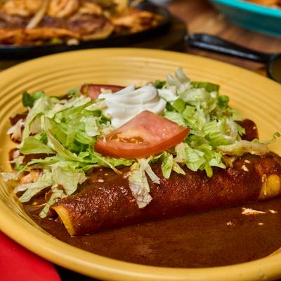Enchiladas in mole sauce served with lettuce, tomatoes, and sour cream.