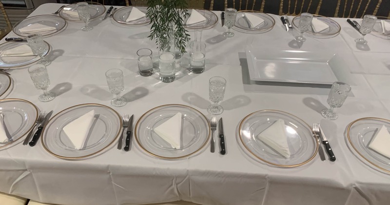 A dining table with glass plates, black-handled cutlery, crystal glasses and a floral centerpiece.
