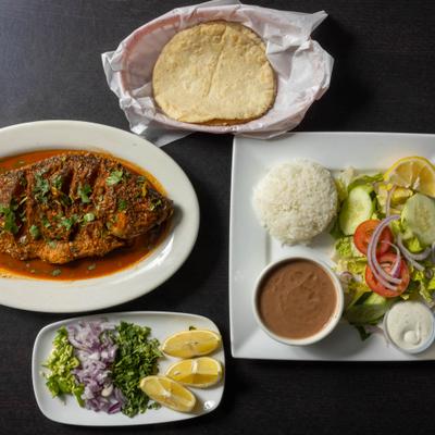 Fried whole fish served with salad, beans, rice, tortillas, cilantro, chopped onions, and jalapenos.