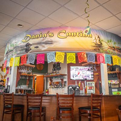A curved bar decorated with a tropical mural banner, papel picado flags, and bar stools.